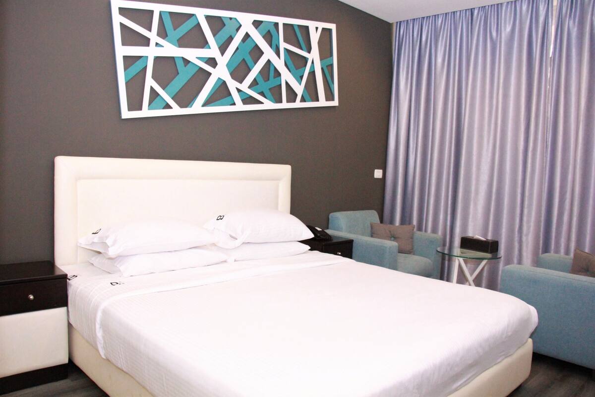 A hotel room with a large bed, a bedside table, a chair, and a small table.