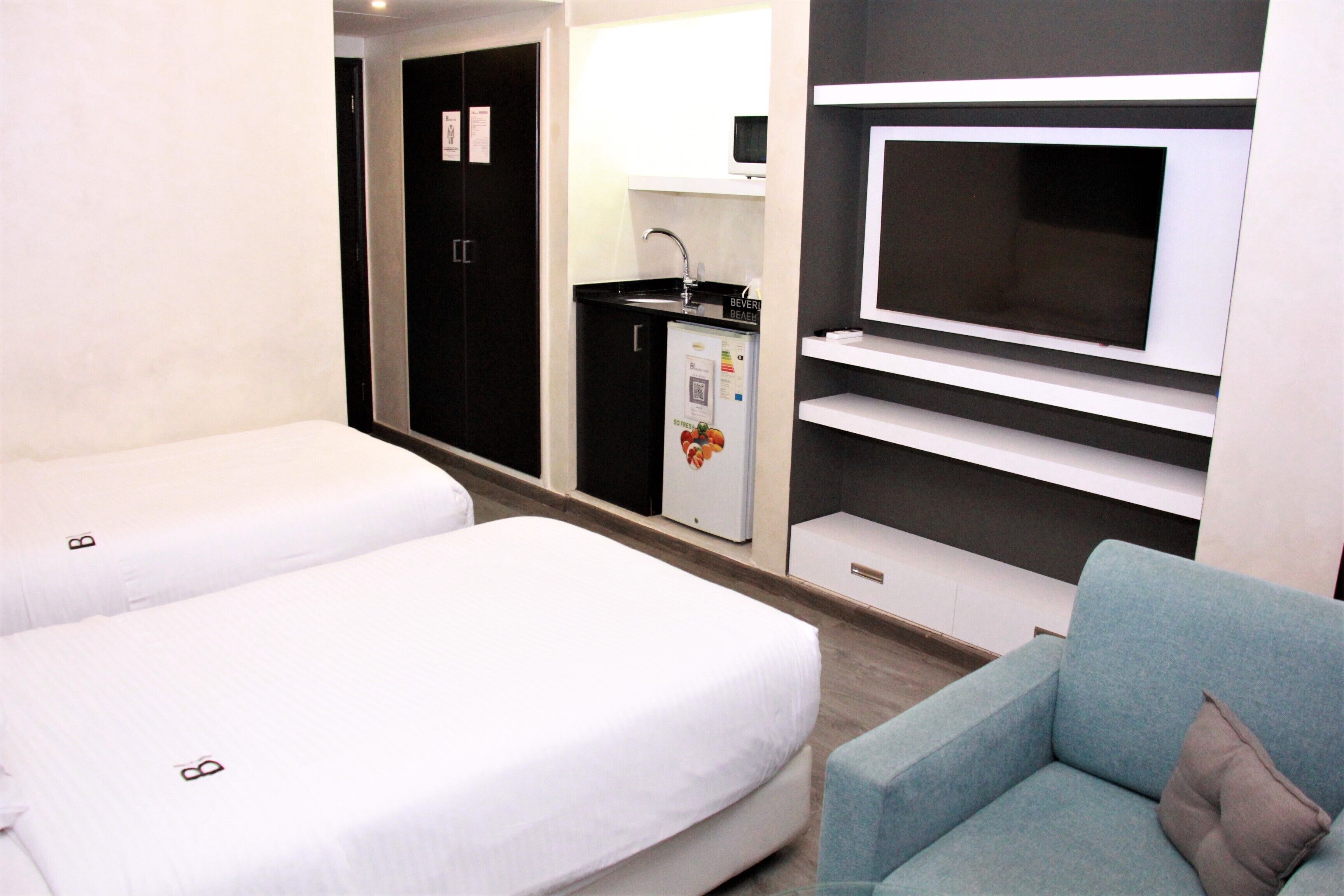 Habitación de hotel con dos camas individuales, kitchenette, televisión y zona de estar.