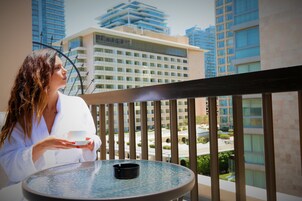 A person seated at a round table on a balcony with a view of high-rise buildings.