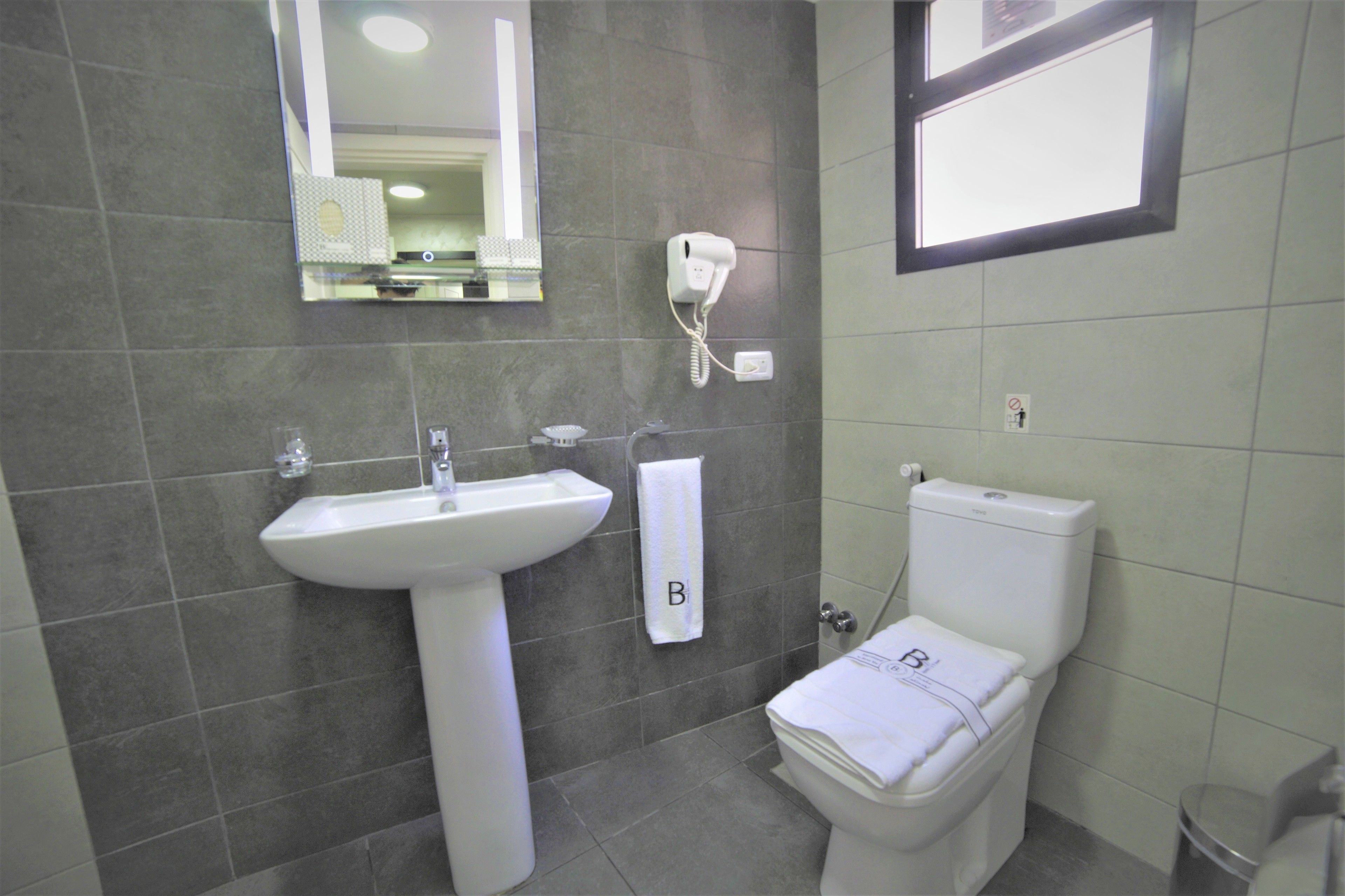A bathroom with a white sink, a toilet, and a hairdryer mounted on the wall.