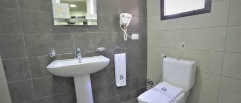 A bathroom with a white sink, a toilet, and a hairdryer mounted on the wall.