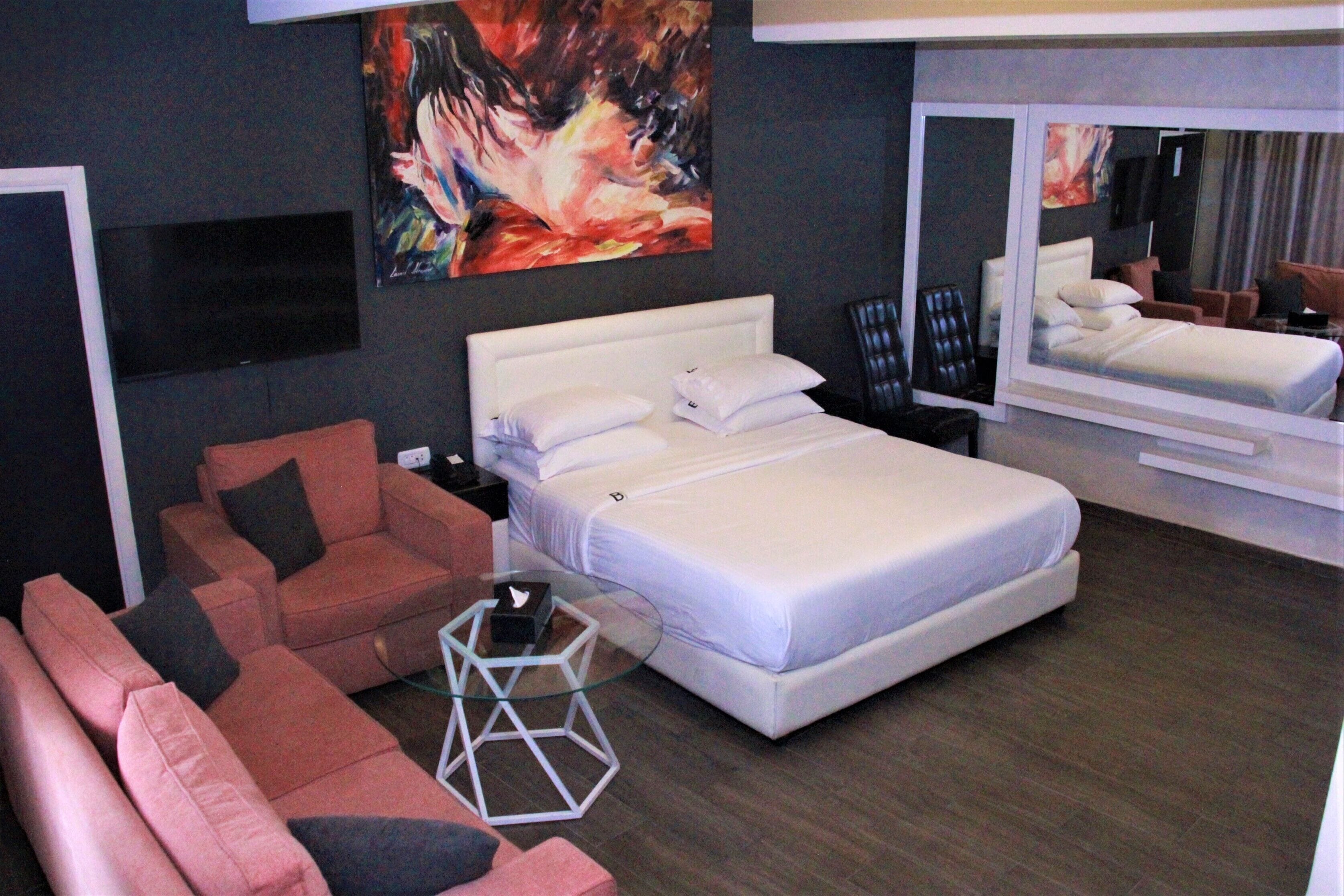Una habitación de hotel moderna con una cama grande, un sofá, una mesa de centro de vidrio y un cuadro en la pared.