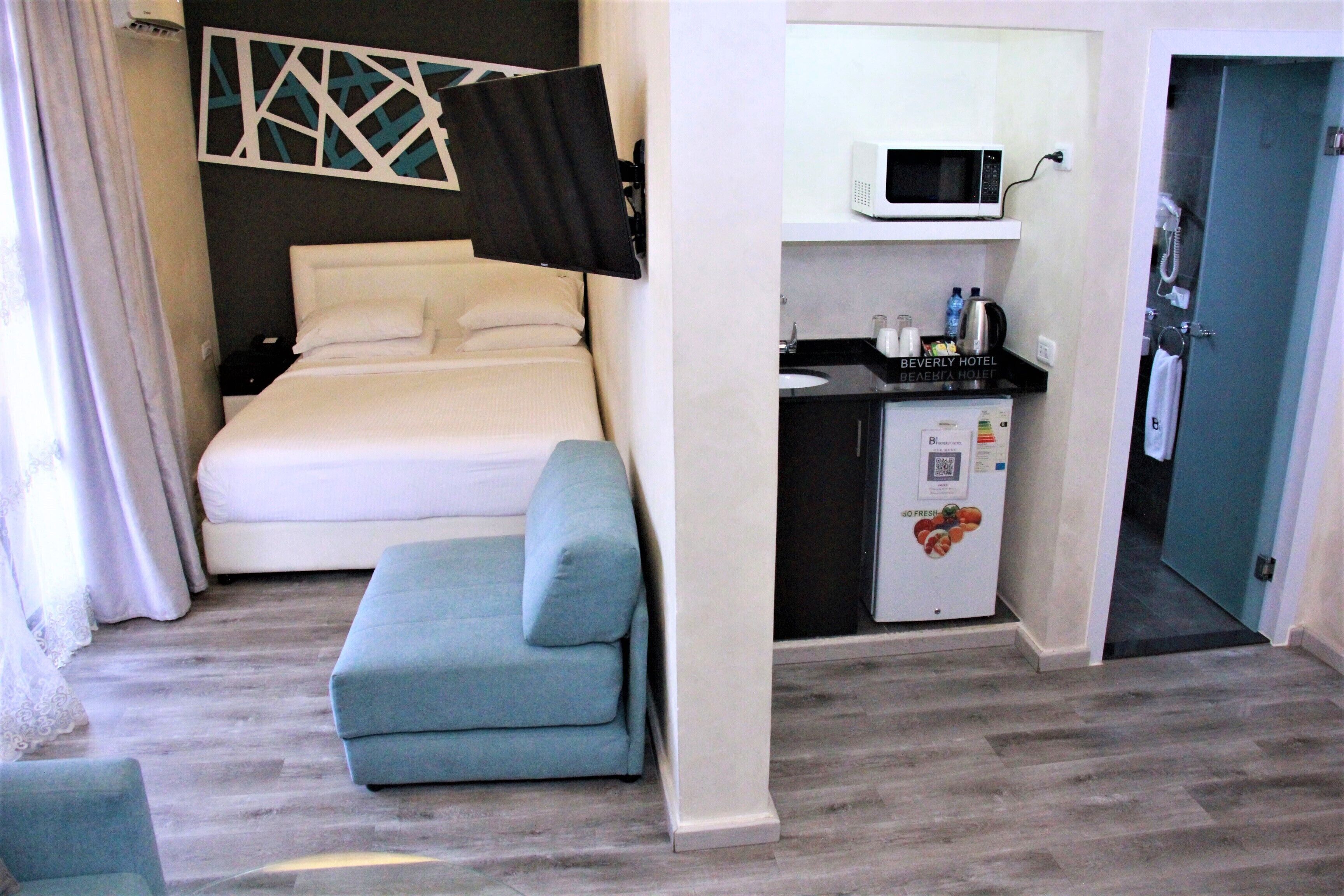 Una camera d'albergo compatta con un letto, un angolo cottura, un forno a microonde e un accesso al bagno.