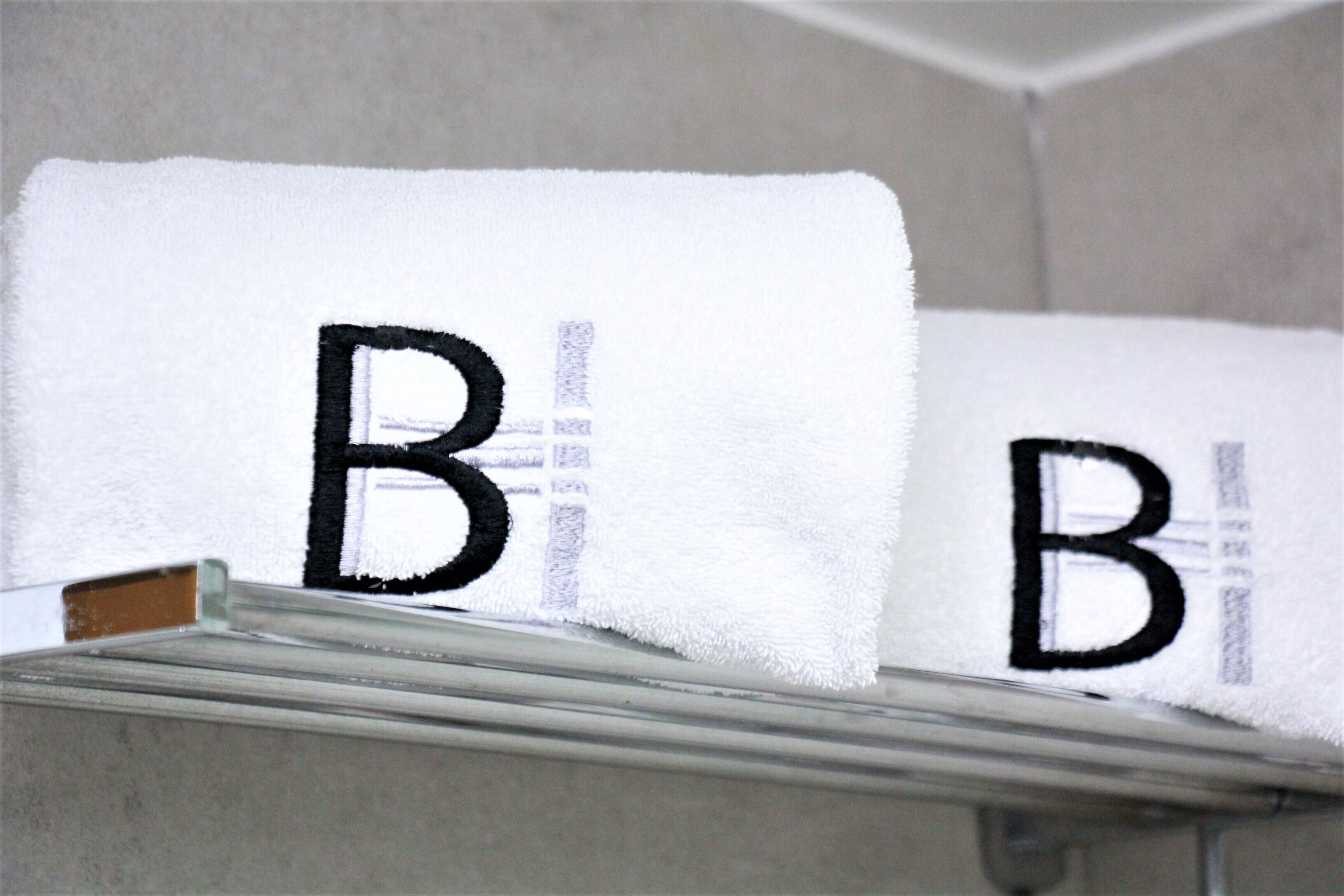 A white towel with the letter "B" embroidered on it, hanging on a metal rack.