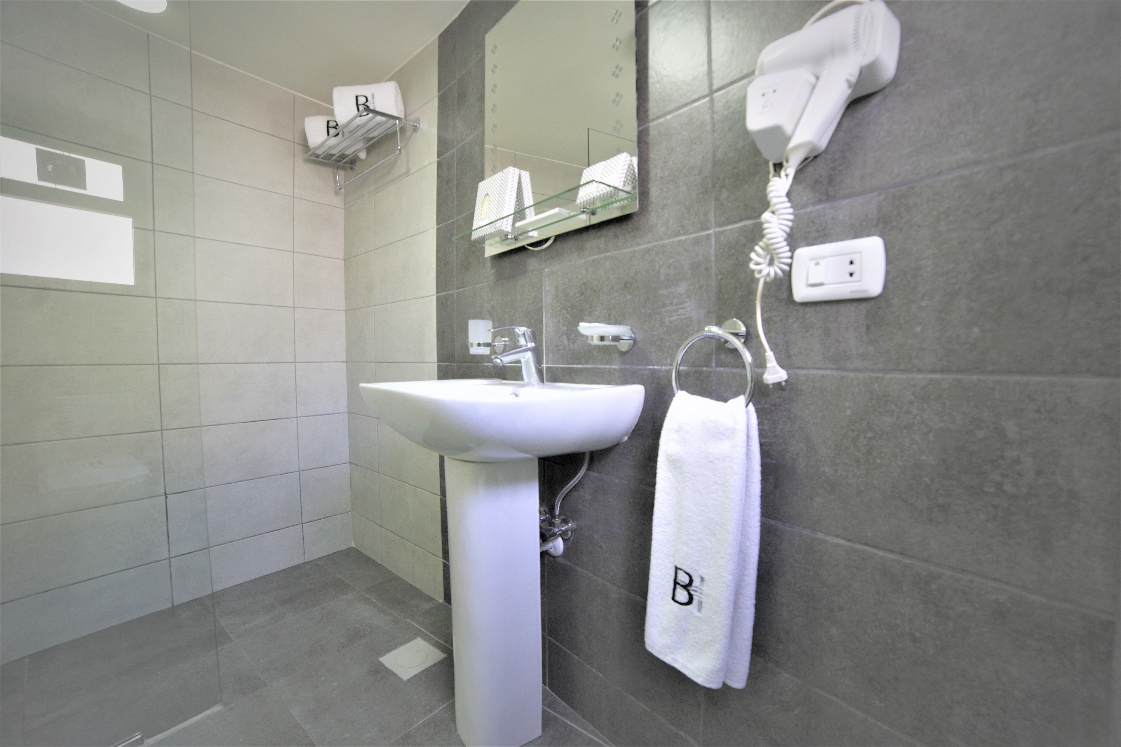Een moderne badkamer met een wit wastafelmeubel, een handdoekrek met een handdoek, een haardroger en een spiegel.