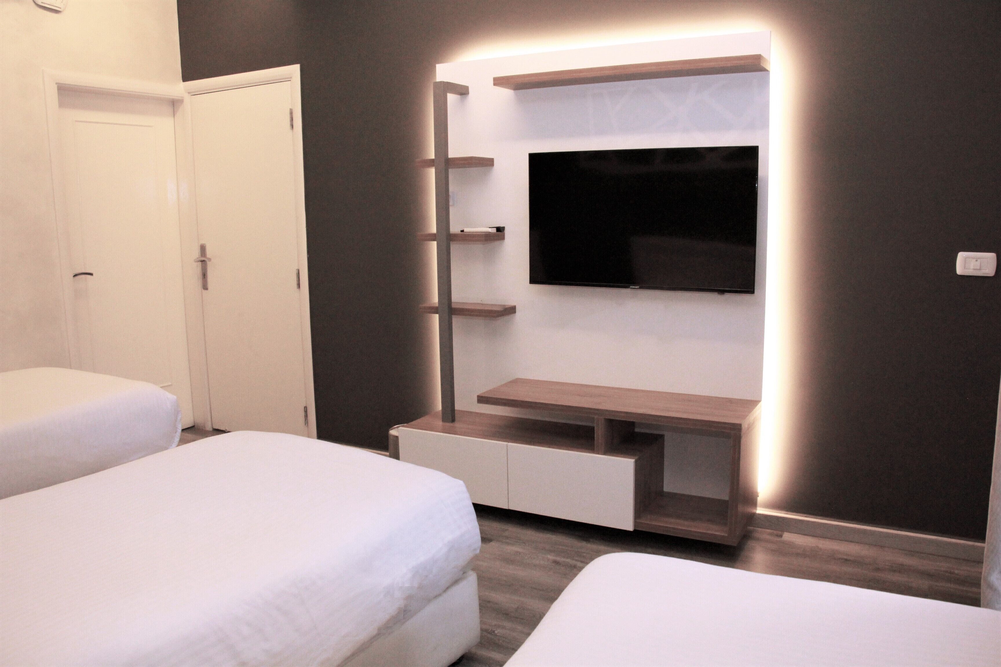 Una habitación de hotel moderna con una gran televisión de pantalla plana montada en la pared, un escritorio integrado con espacio de almacenamiento y dos camas con ropa blanca.