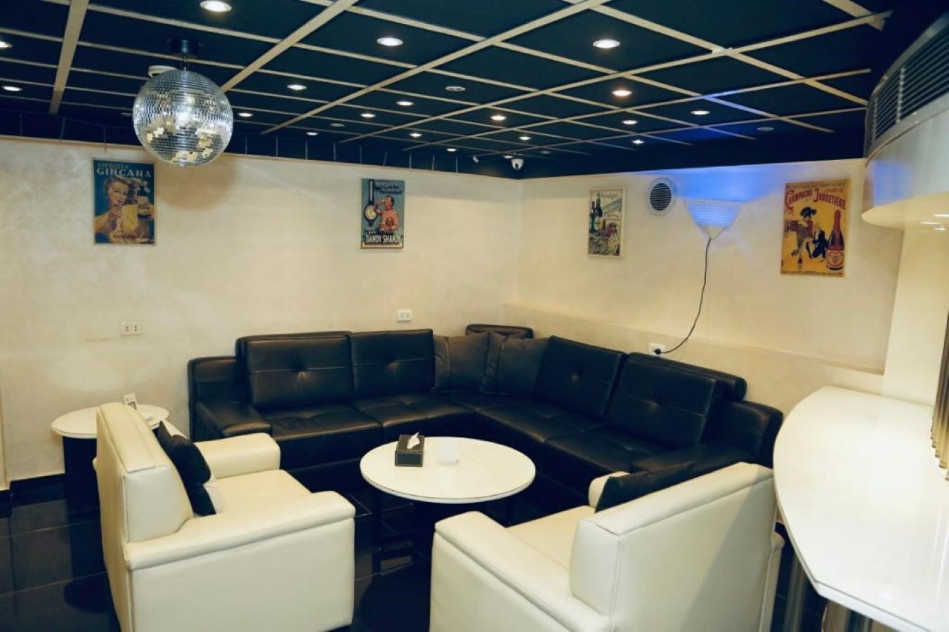 Un área de estar moderna con un sofá seccional de cuero negro, sillones blancos y una mesa de centro redonda.