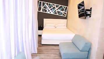 Un dormitorio con cama, sofá azul, mesita de noche y televisión instalada en la pared.
