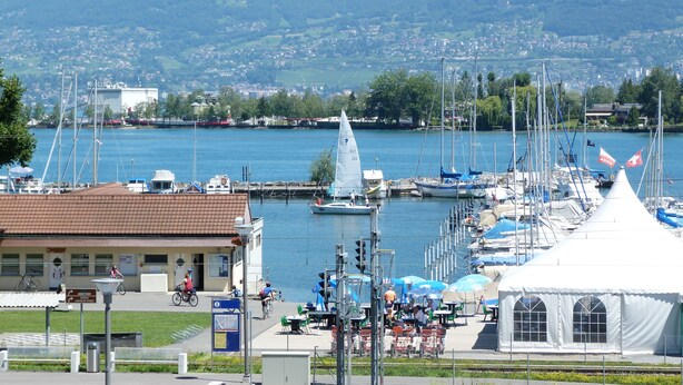 Un porto turistico con barche, un caffè e vista sul lago e sulle montagne.