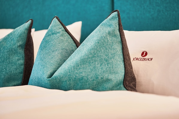 Una cama con almohadas verde agua y blancas, y una almohada blanca con un logotipo.