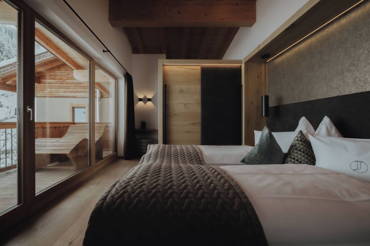A modern bedroom with a large bed, a view through a sliding glass door, and a wooden ceiling.