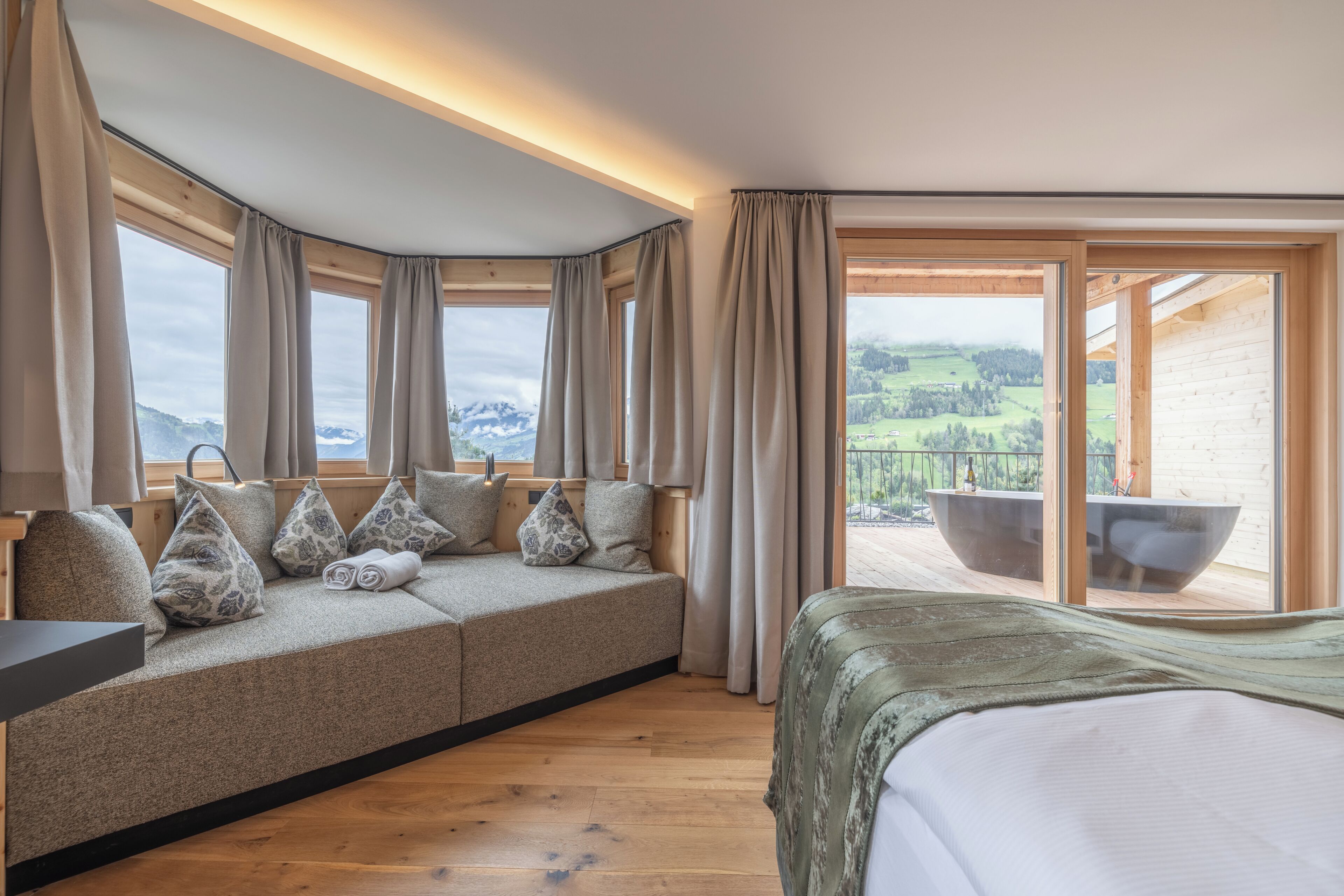A room with a sofa, a bed, and a view of a balcony with a hot tub.