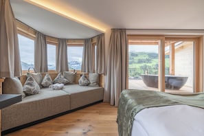 A room with a sofa, a bed, and a view of a balcony with a hot tub. - Ferienhotel Jörglerhof (Hainzenberg)