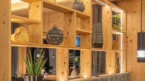 Un interior moderno con una estantería de madera que exhibe objetos decorativos, un banco tapizado en gris y una mesa de madera con un florero y cristalería.