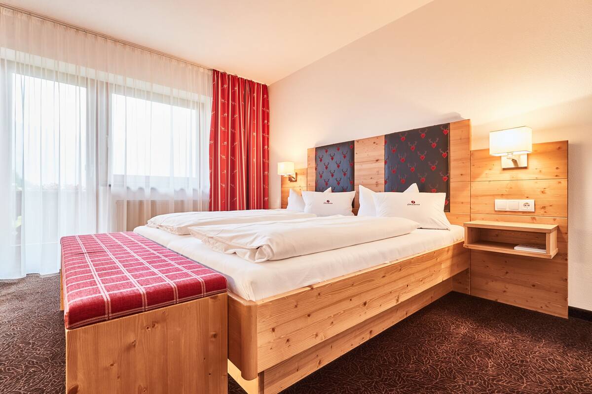 A hotel room with a wooden bed, a bench, a nightstand, and a wall-mounted lamp.