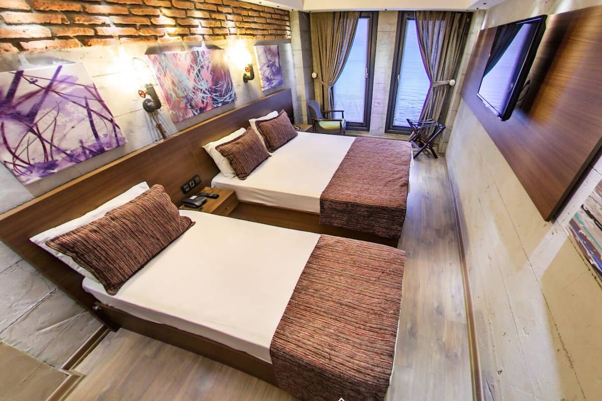 A modern hotel room with two beds, a brick wall, artwork, and a TV.