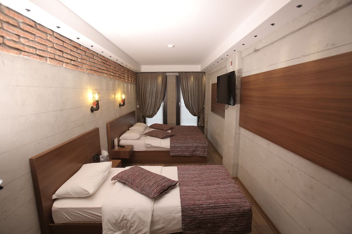 A hotel room with two beds, a brick wall, a flat-screen TV, and a window with curtains.