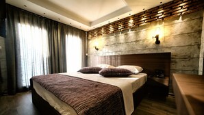 A modern hotel room with a large bed, dark wood flooring, a brick-patterned headboard, and a large window with curtains.