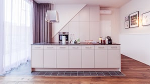 Eine moderne Küche mit einer zentralen Kochinsel, weißen Schränken und einem großen Fenster mit transparenten Vorhängen.