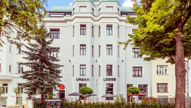 Ein weißes Gebäude mit der Beschilderung "URBAN LODGE", das eine symmetrische Fassade mit gleichmäßig verteilten Fenstern und einem zentralen Eingang zeigt.