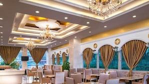 A spacious hotel lobby with seating areas, chandeliers, and large windows with curtains.
