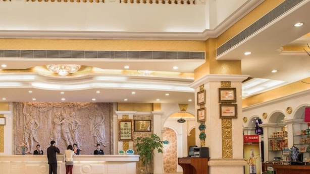 A grand lobby with a marble reception desk, a chandelier, and a balcony with ornate railings.
