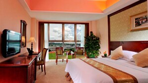 A hotel room with a large bed, a desk with a television, a chair, a small table, and a large window offering a view.