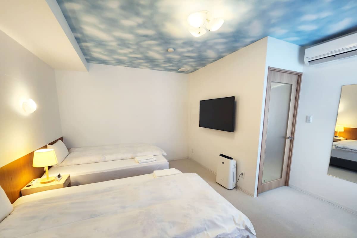 Habitación de hotel con dos camas, un televisor de pantalla plana montado en la pared, un techo con diseño de nubes y un equipo de aire acondicionado.