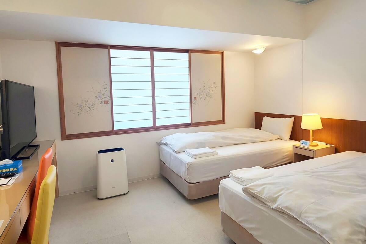 Habitación de hotel con dos camas, un escritorio con una silla, un televisor y un techo con diseño de nubes.