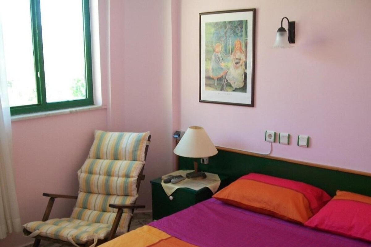 A room with a bed, a chair, a lamp, and a painting on the wall.