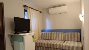 Un espace de vie compact avec un téléviseur posé sur un petit meuble blanc, un canapé à rayures et un appareil de climatisation fixé au mur.