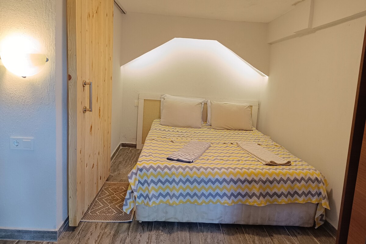 A small, cozy bedroom with a bed, a wooden wardrobe, and a ceiling light.