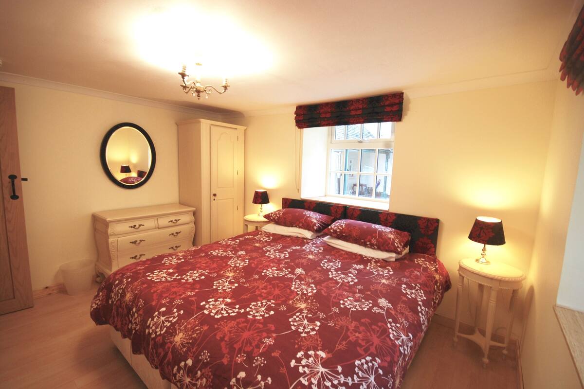 A bedroom with a large bed, a dresser, a mirror, a window with curtains, and two bedside lamps.