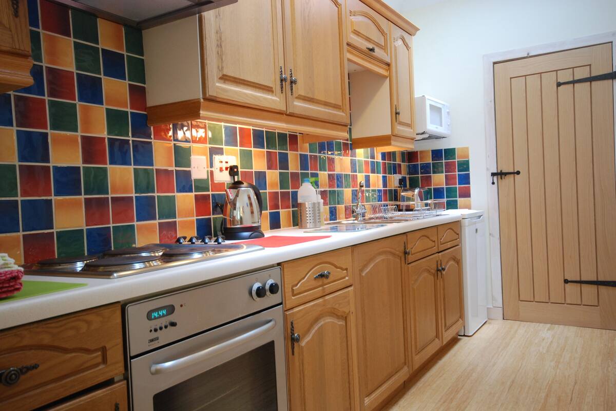 A kitchen with wooden cabinets, a microwave, a stove, and colorful tiles on the backsplash.