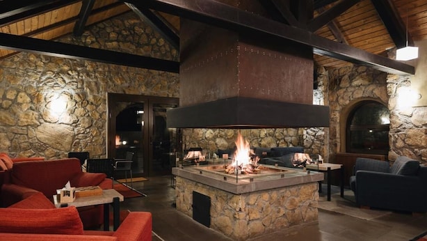 A stone fireplace with a fire, surrounded by red sofas and a stone wall. - Tufenkian Avan Marak Tsapatagh Hotel (Tsapatagh)