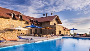 Ein Steinhaus mit Schwimmbad, Liegestühlen und Sonnenschirmen.