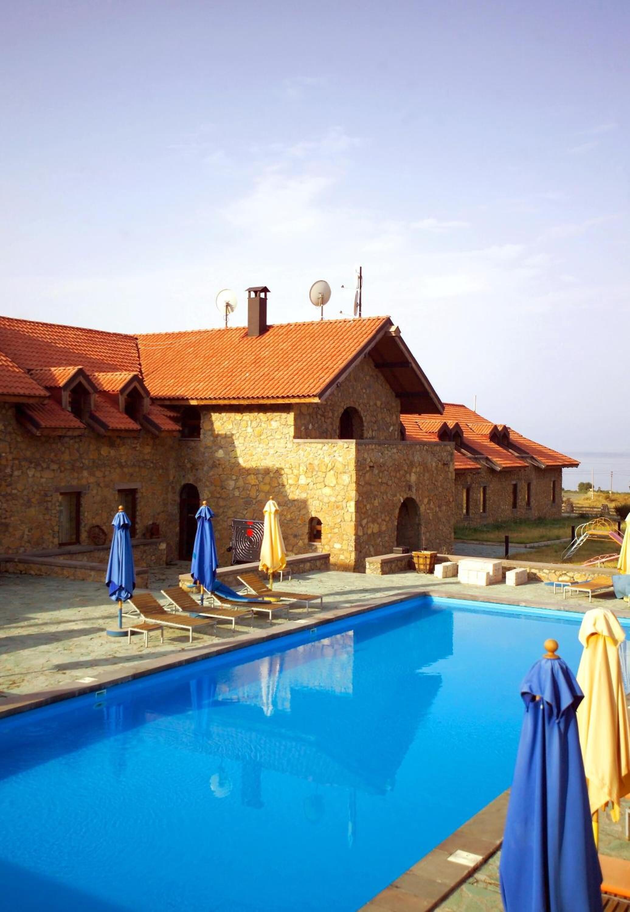A stone building with a swimming pool, outdoor umbrellas, and lounge chairs.