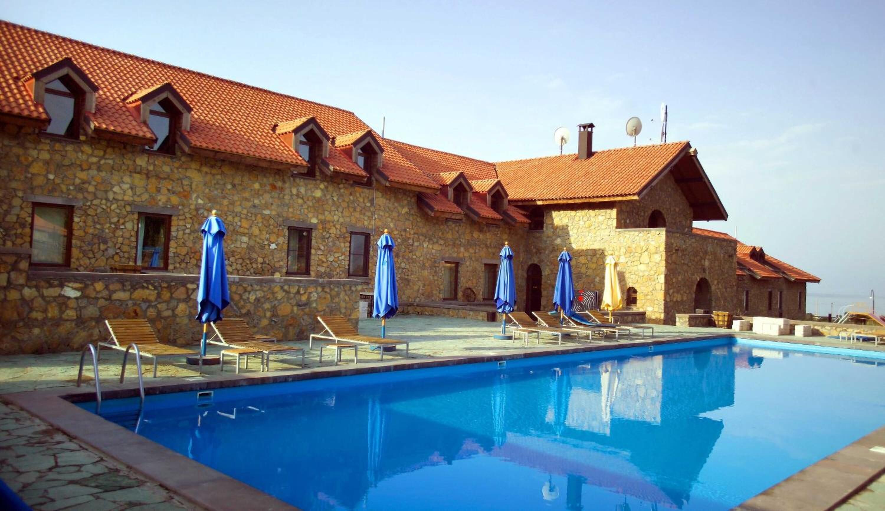 A stone building with a swimming pool, blue umbrellas, and lounge chairs.