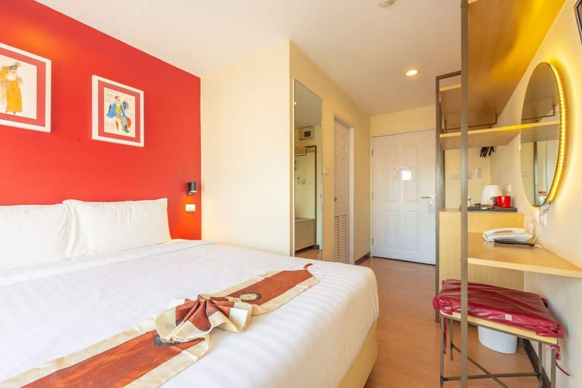 A hotel room with a large bed, a desk with a mirror, and a red accent wall.