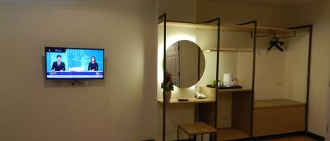 Habitación de hotel con televisión, escritorio con espejo, un taburete pequeño, cama y armario.