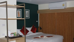 A hotel room with a bed, a desk with a tray of toiletries, a wall-mounted air conditioner, and a curtain. - Klean Residence Hotel (Bangkok)