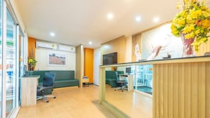 A reception area with a wooden reception desk, green seating, and a large window. - Klean Residence Hotel (Bangkok)
