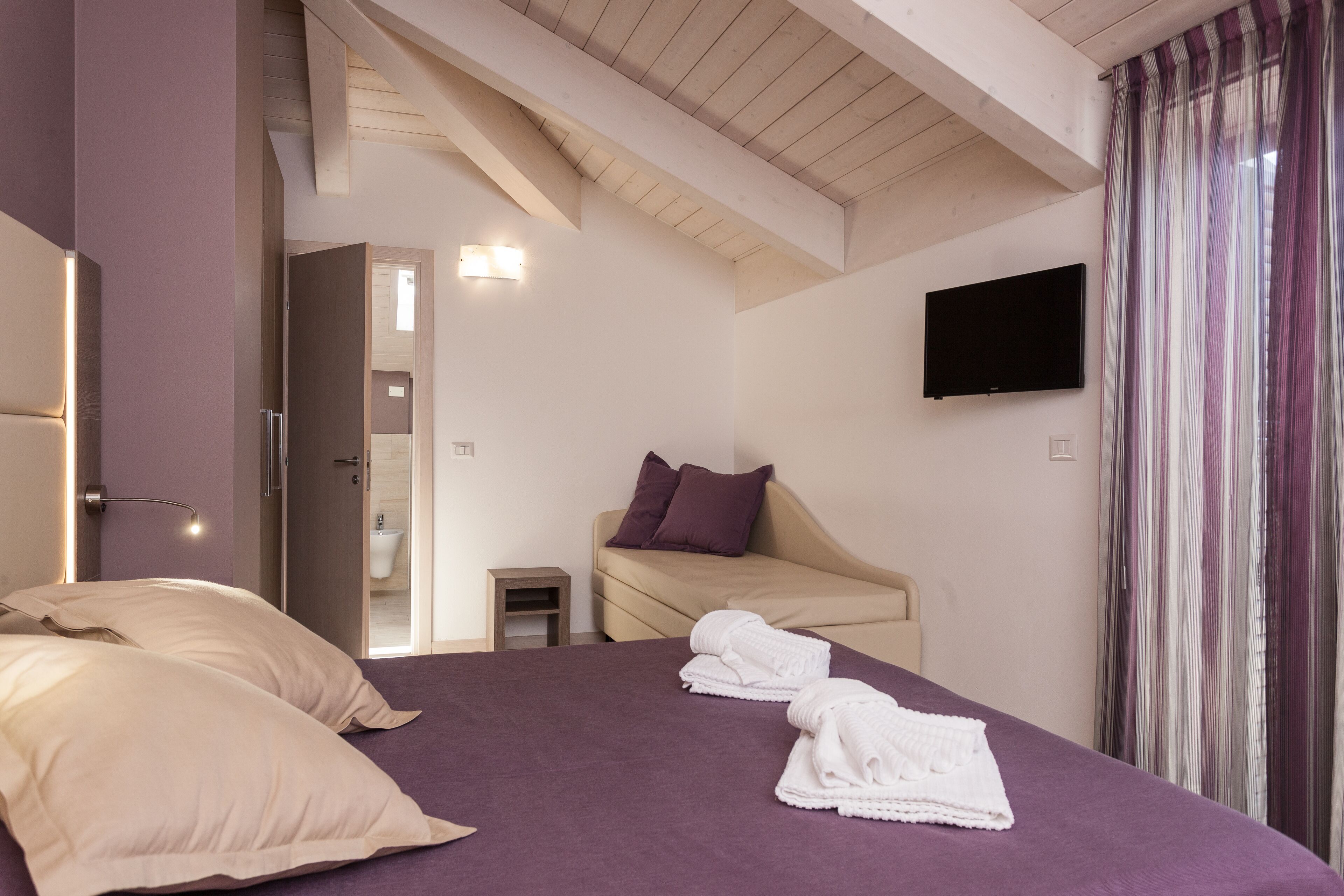 Une chambre à coucher avec un lit, une télévision et une salle de bain visible à travers une porte ouverte.