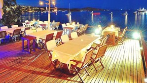 An outdoor dining area with tables and chairs, a decorative tree with lights, and a view of the sea at night. - Beste Hotel (Bodrum)