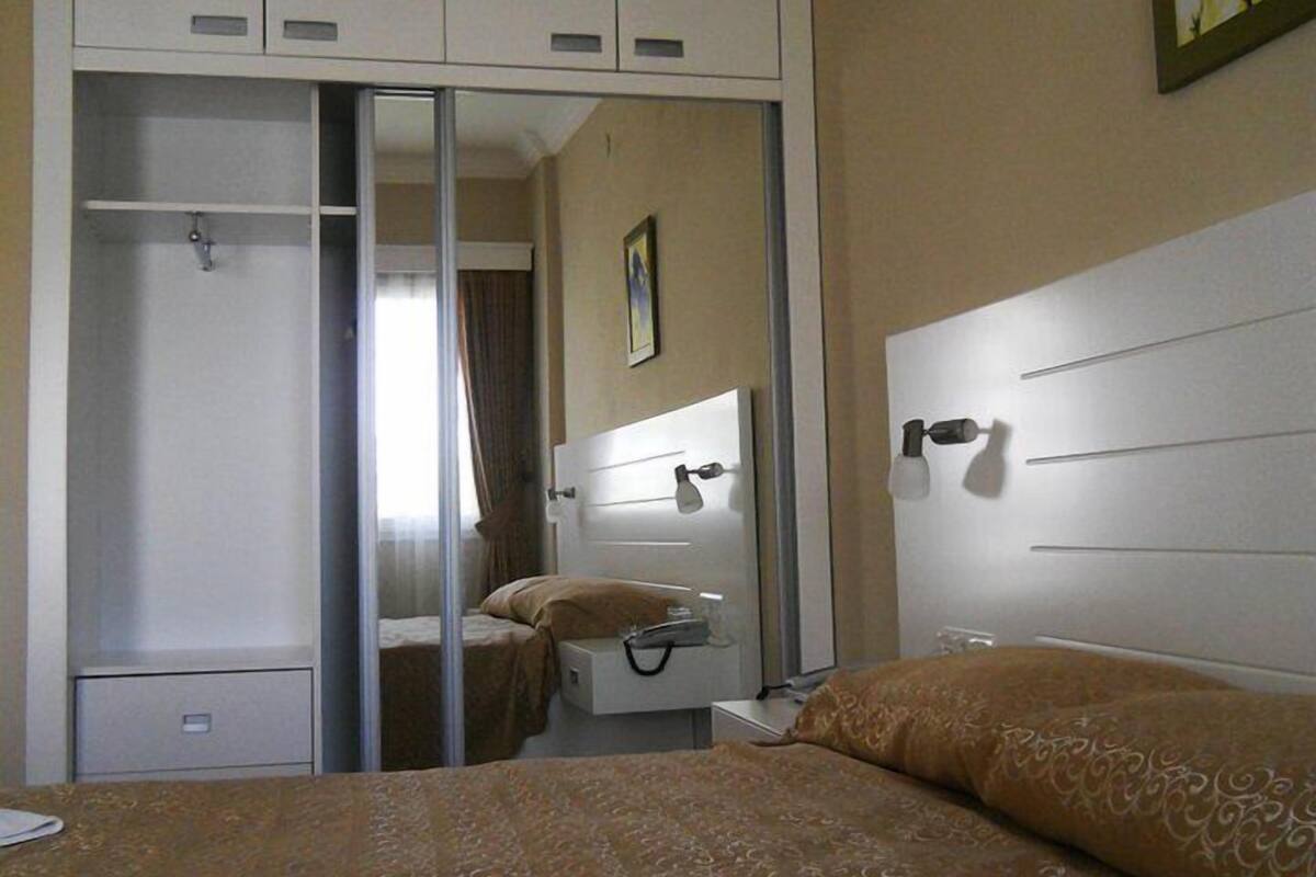 Habitación de hotel con cama, mesita de noche, armario con espejo y ventana con cortinas.
