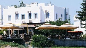 A white building with multiple windows and air conditioning units, outdoor seating with umbrellas, and a garden area. - Beste Hotel (Bodrum)
