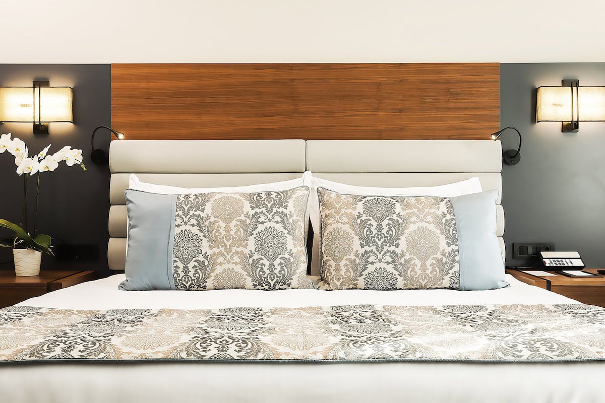 A bedroom with a double bed, two nightstands, a wall-mounted lamp, and a potted plant.