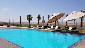 A rectangular swimming pool with clear blue water, surrounded by wooden deck and lounge chairs with umbrellas. - Dedeman Cizre (Cizre)