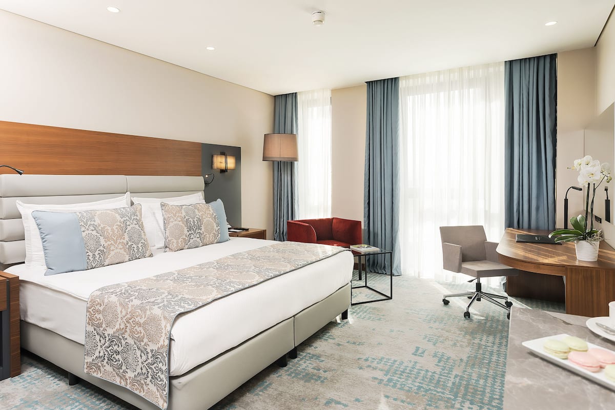 A hotel room with a large bed, a desk, a chair, and a small table with a plant.