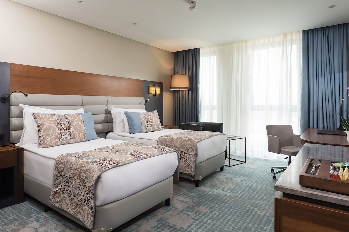 A hotel room with two beds, a desk, a chair, a lamp, and a potted orchid.